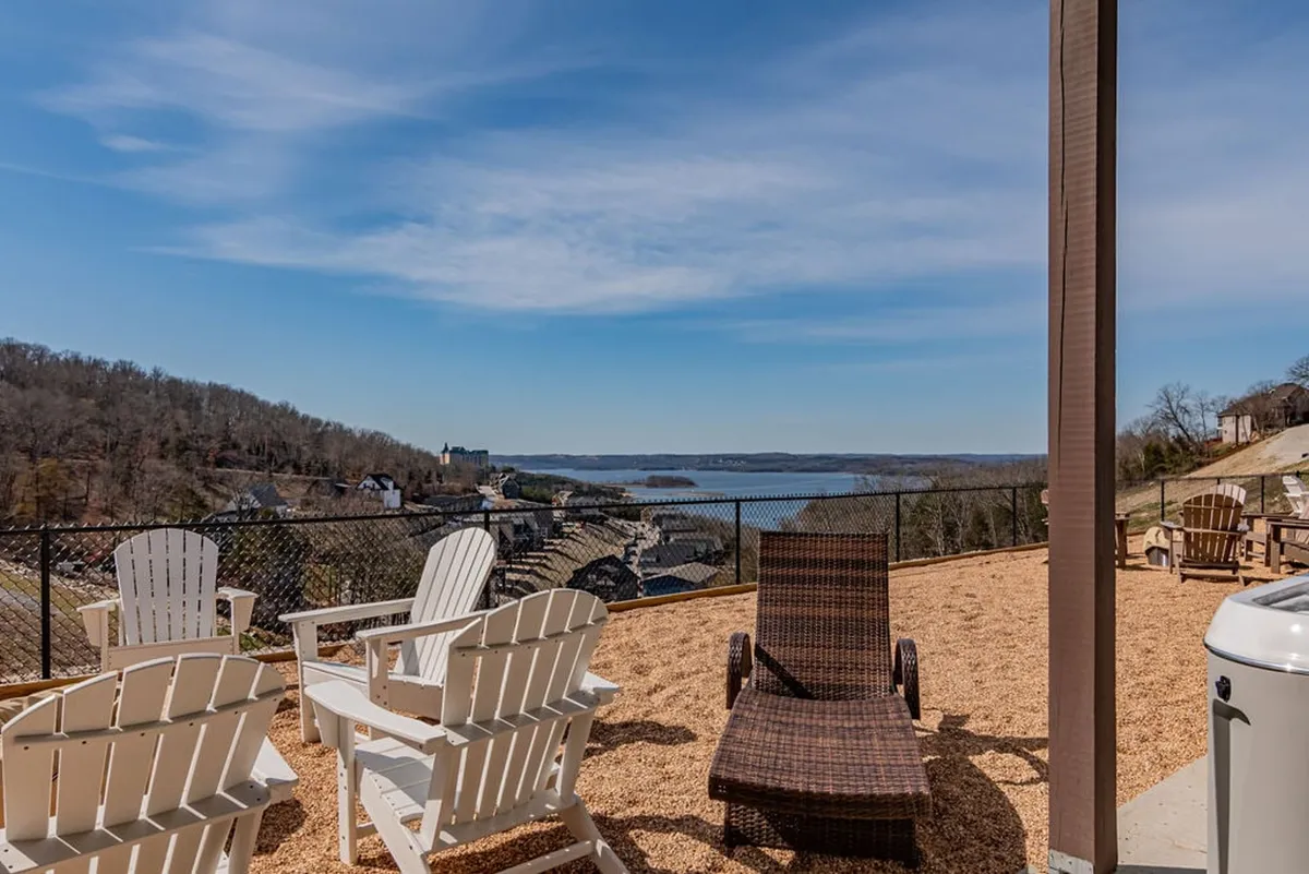 This exterior image features a row of Adirondack chairs overlooking a serene lake, with rolling hills in the background. The tranquil setting emphasizes the connection to nature and the peacefulness of the environment surrounding the property.