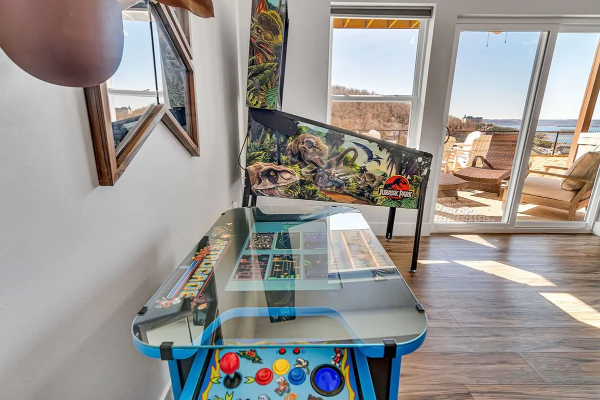A vibrant game lounge featuring a classic pinball machine and an arcade game table, set beside large windows that offer natural light and a scenic view. The room is styled for relaxation and fun, ideal for socializing and friendly competition.