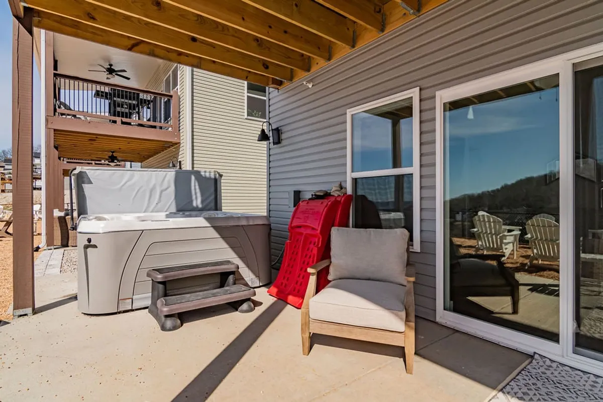 An inviting outdoor deck featuring a bubbling hot tub, several adirondack chairs, and cozy seating with a view of the tranquil lake beyond. The scene is perfect for relaxing under the stars or socializing with friends while enjoying nature.