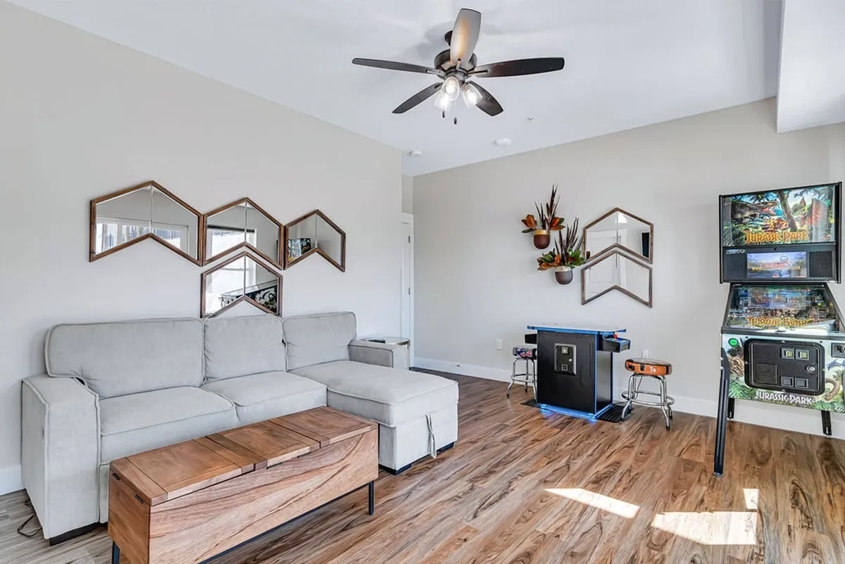 A casual, playful interior featuring a sofa, coffee table, mirrors, and a retro arcade game. The space is arranged for relaxation and group activities, with décor that feels bright and welcoming for all ages.