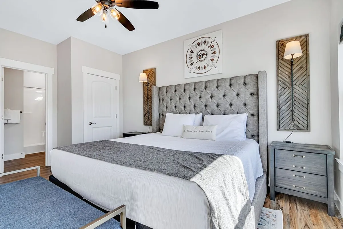 A King suite with a tufted headboard, warm decorative wall art, nightstands, and soft lighting that creates an inviting, cozy atmosphere. Natural light filters gently through the window, highlighting thoughtful, elegant details.
