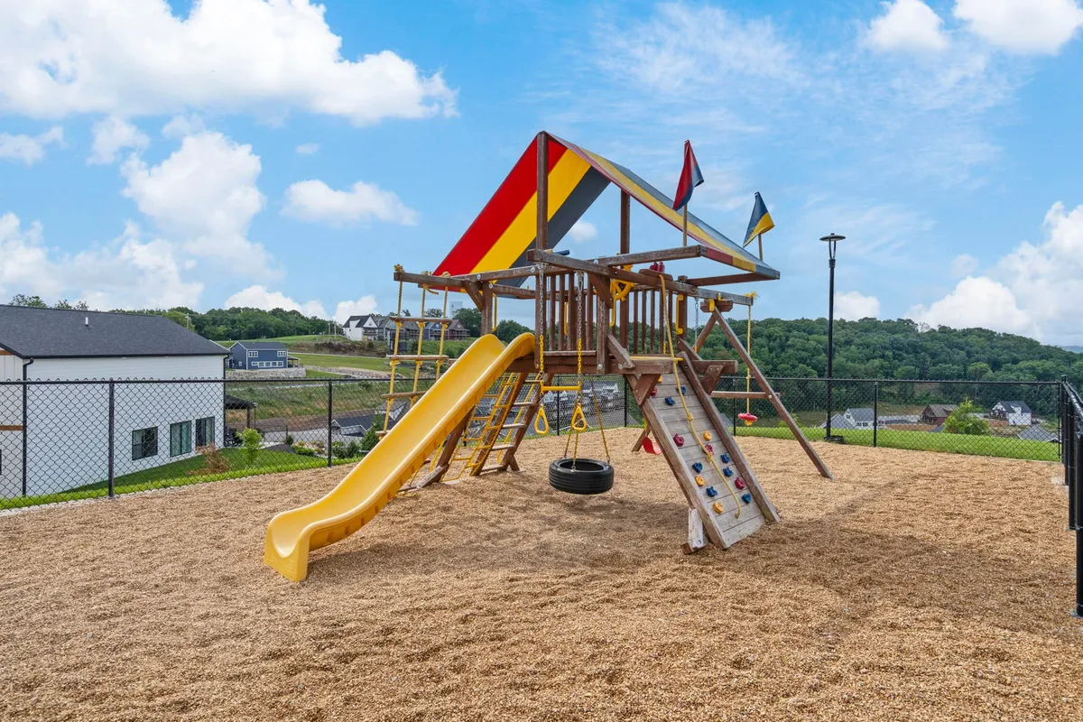 An exterior shot of a cheerful playground structure with a yellow slide and swing set, surrounded by green space. Children are seen playing, evoking carefree family gatherings and outdoor fun.