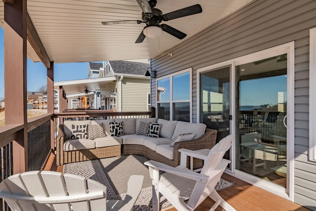 An inviting exterior lounge space with a curved sectional sofa, Adirondack chairs, and decorative pillows. Surrounded by serene greenery and equipped with a ceiling fan, the space is ideal for outdoor comfort and relaxation while enjoying the lake views or evening breezes.
