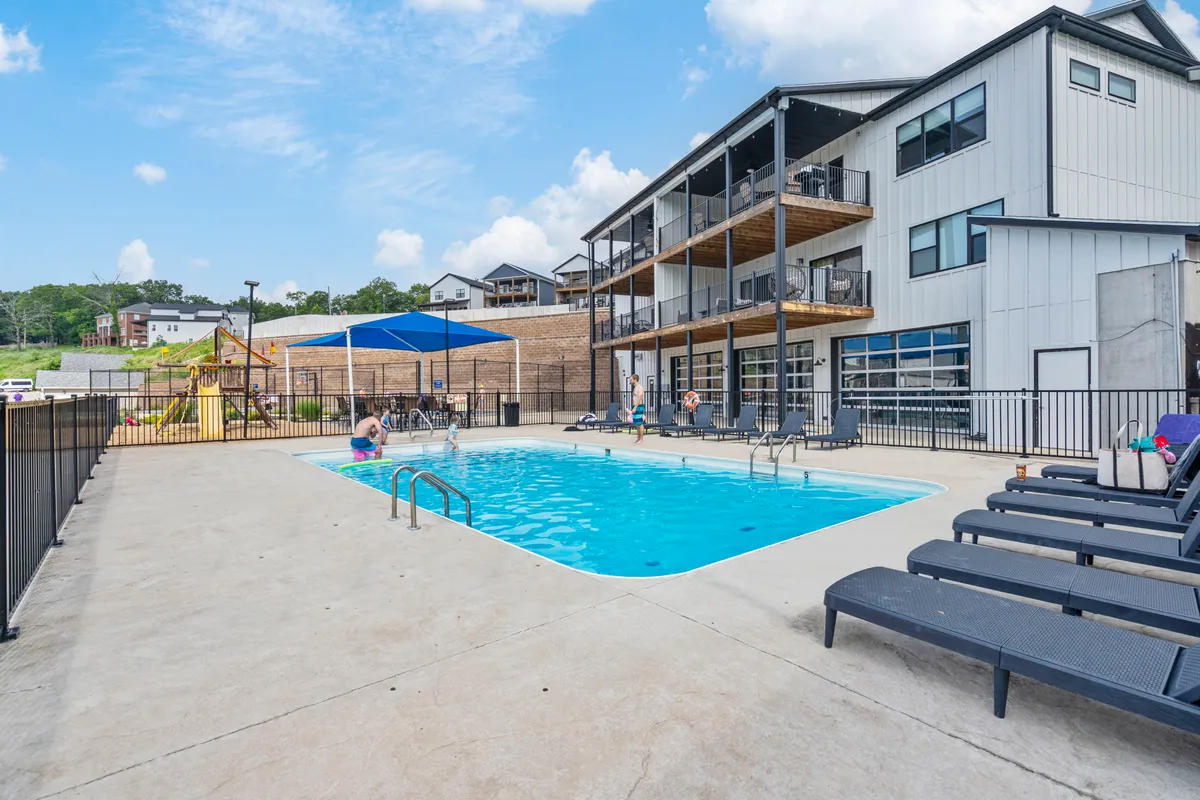 A relaxed exterior scene with a swimming pool, lounge chairs, and balconies. The open-air environment encourages outdoor relaxation and activities, promoting healthy, clean living in a well-maintained communal space.