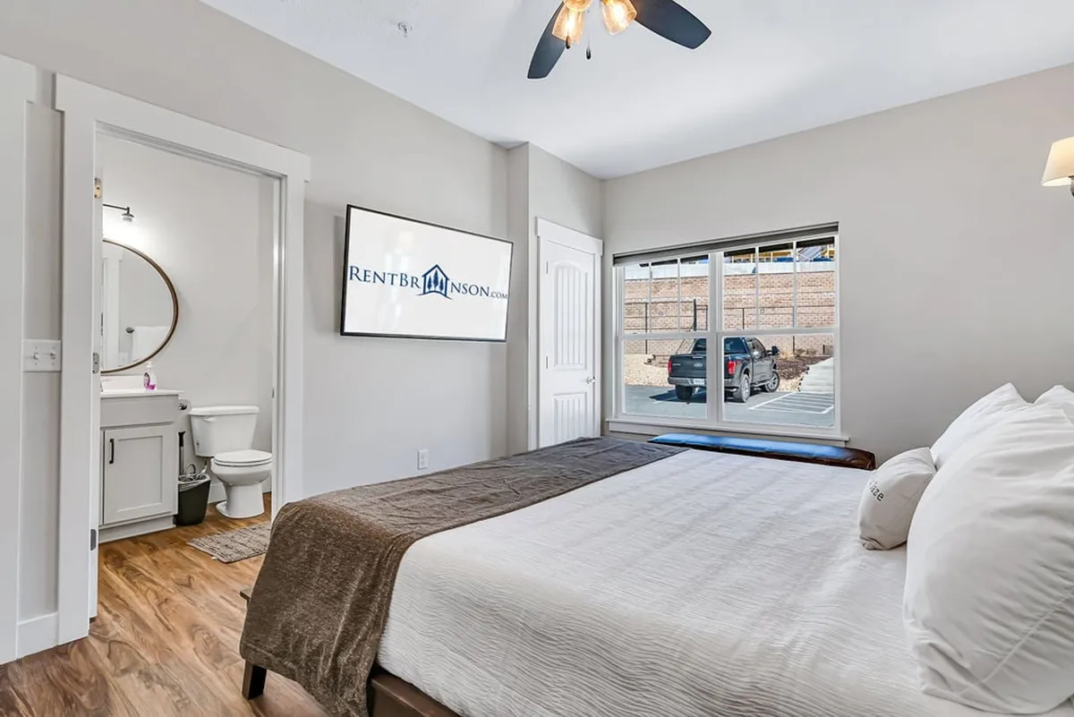 A King bedroom with a plush neutral-toned bed, large window with a view, and a wall-mounted 55" Sony TV. The room feels airy and comfortable, with contemporary touches and a layout that emphasizes both relaxation and entertainment.