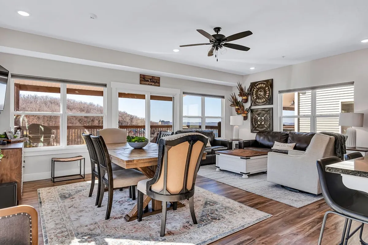 The image showcases a warm, inviting open-concept living and dining area with a spacious dining table, plush sofa, and large windows that bathe the space in natural light. Tasteful wall art and cozy decor create a welcoming atmosphere, perfect for gatherings.