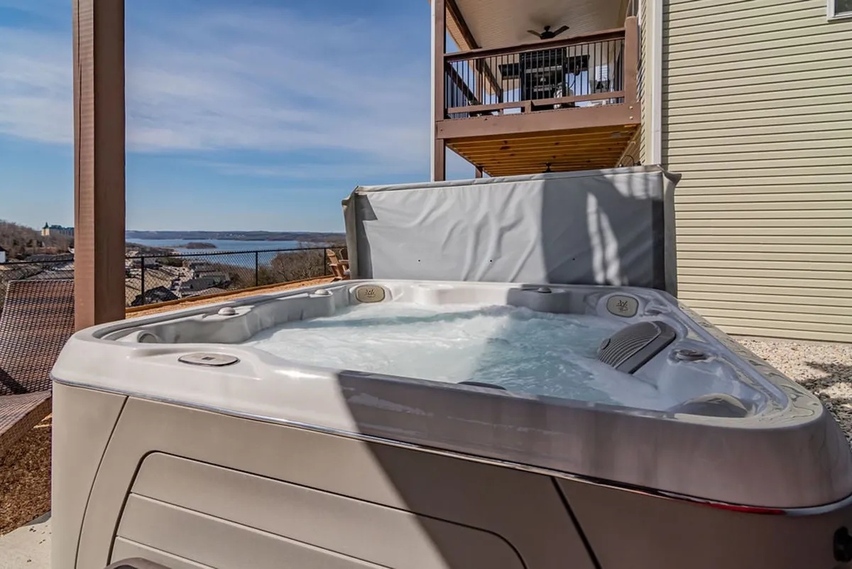 A luxurious hot tub is nestled on a spacious deck overlooking the lake, offering tranquil water views and a serene atmosphere. The setting is ideal for relaxing under the stars or sunbathing during the day.