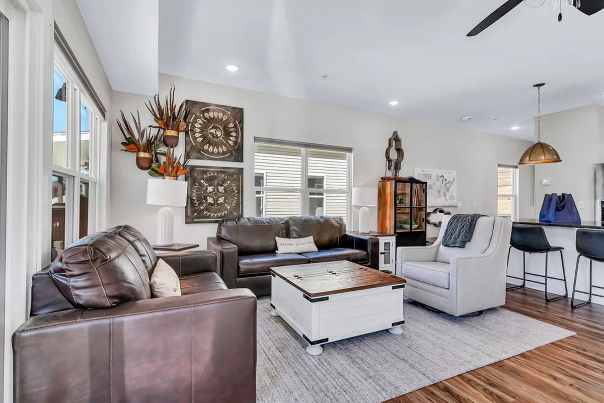 This interior shot highlights a comfortable living area with plush leather sofas, a stylish coffee table, decorative wall art, and warm lighting. The arrangement encourages relaxation, movie nights, and social interaction after a day of adventures.
