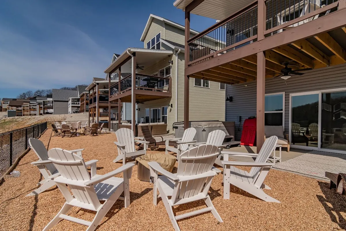 A spacious deck is set up for gatherings, with ample outdoor seating arranged around a glowing fire pit. The multi-level deck design and lake views in the background make it ideal for both daytime games and evening s’mores under the stars.